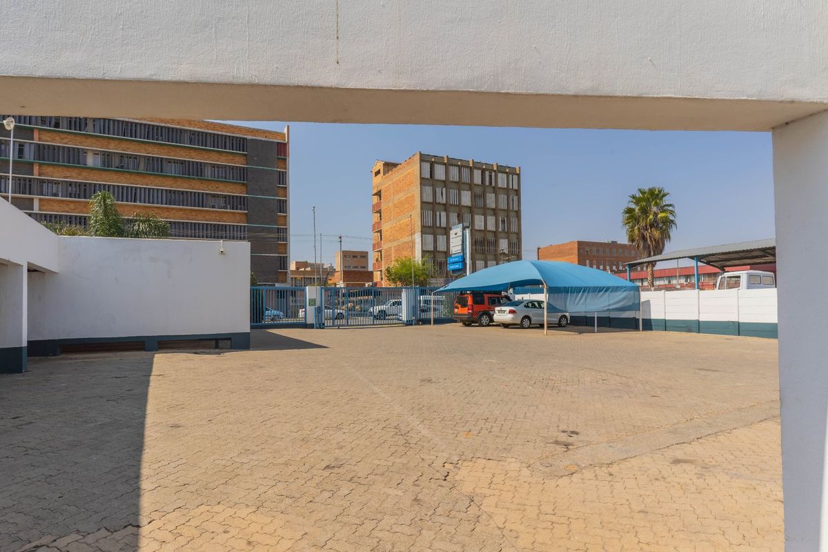 Industrial property exterior featuring a paved parking area, secure metal gate access, and a shade cloth carport structure.