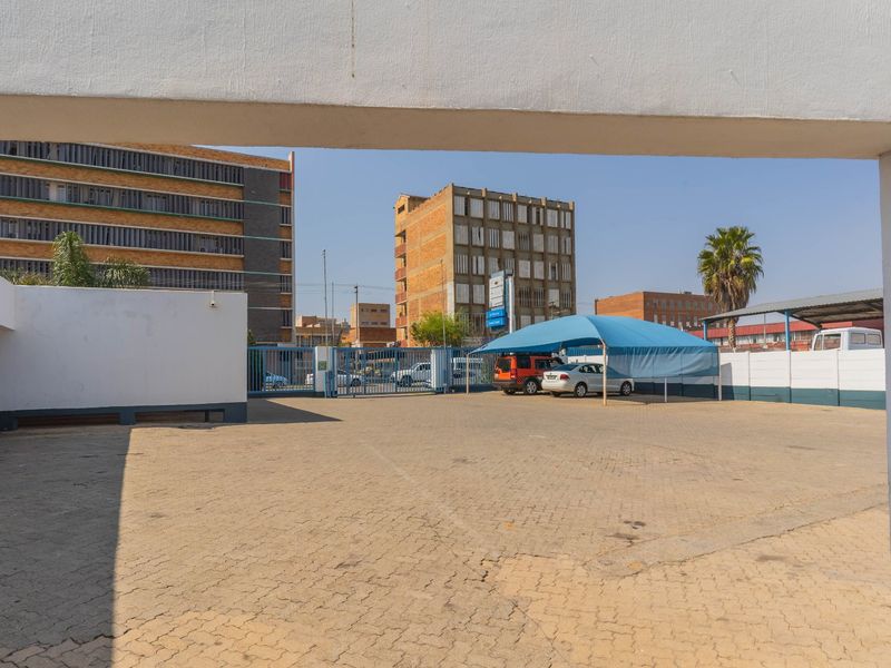 Industrial property exterior featuring a paved parking area, secure metal gate access, and a shade cloth carport structure.