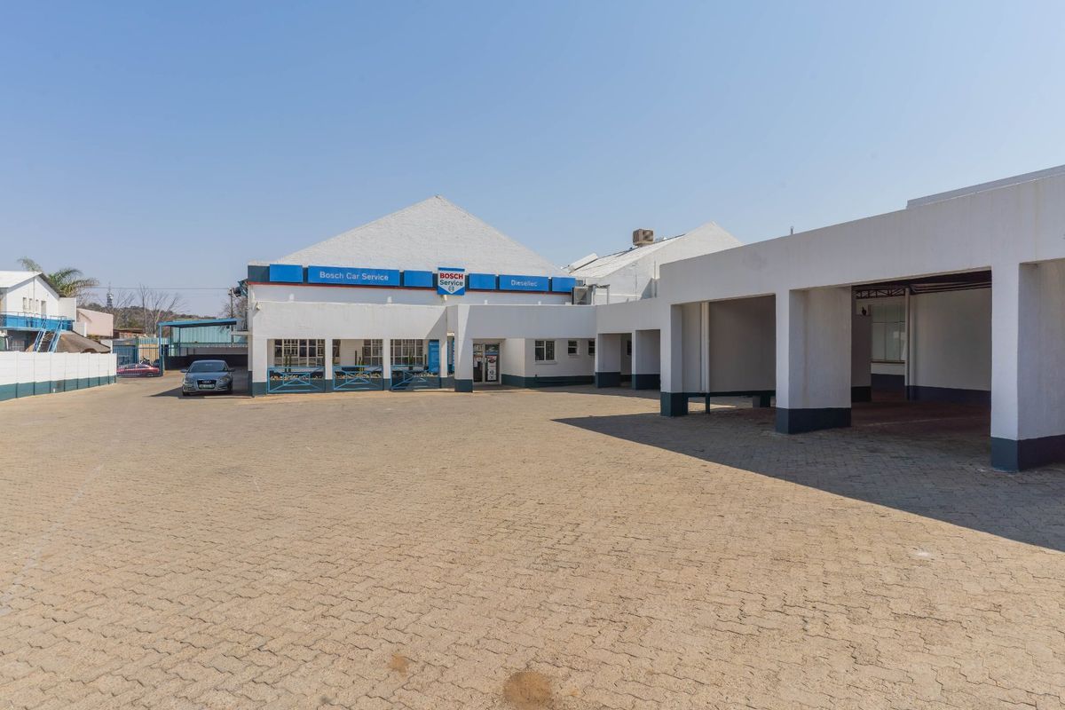 Front exterior view of an industrial property featuring a paved driveway, covered parking bays, and commercial signage.