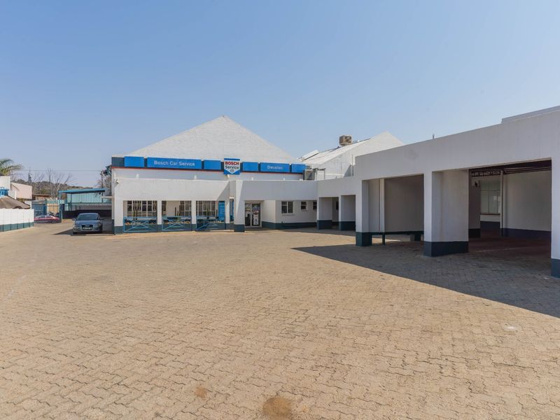Front exterior view of an industrial property featuring a paved driveway, covered parking bays, and commercial signage.