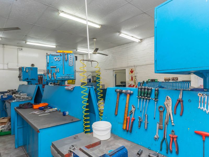 Industrial workshop space featuring built-in metal workbenches, wall-mounted tool storage systems, compressed air lines, and functional overhead fluorescent lighting.
