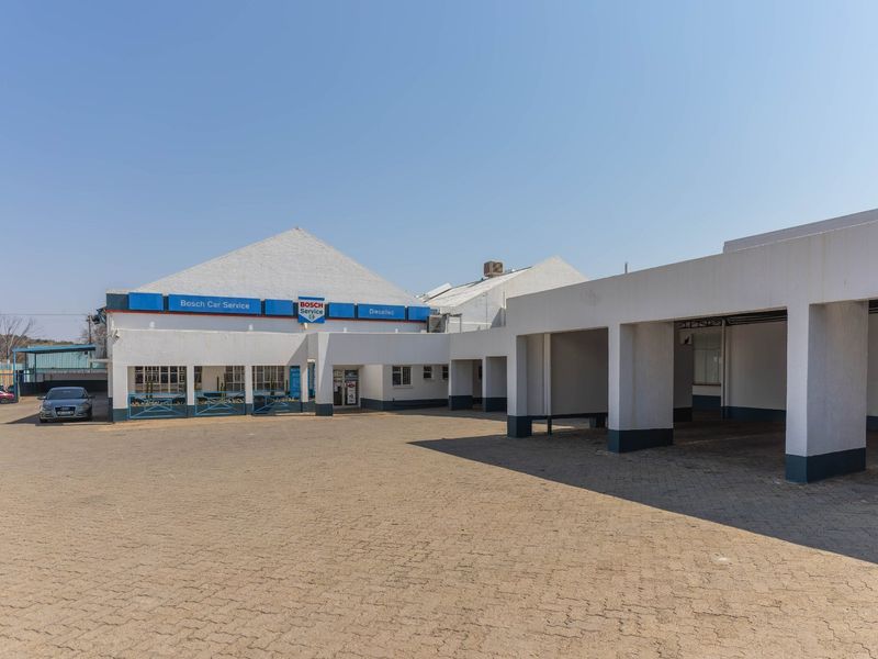 Front exterior view of an industrial property featuring a paved driveway, covered parking bays, and established commercial signage.