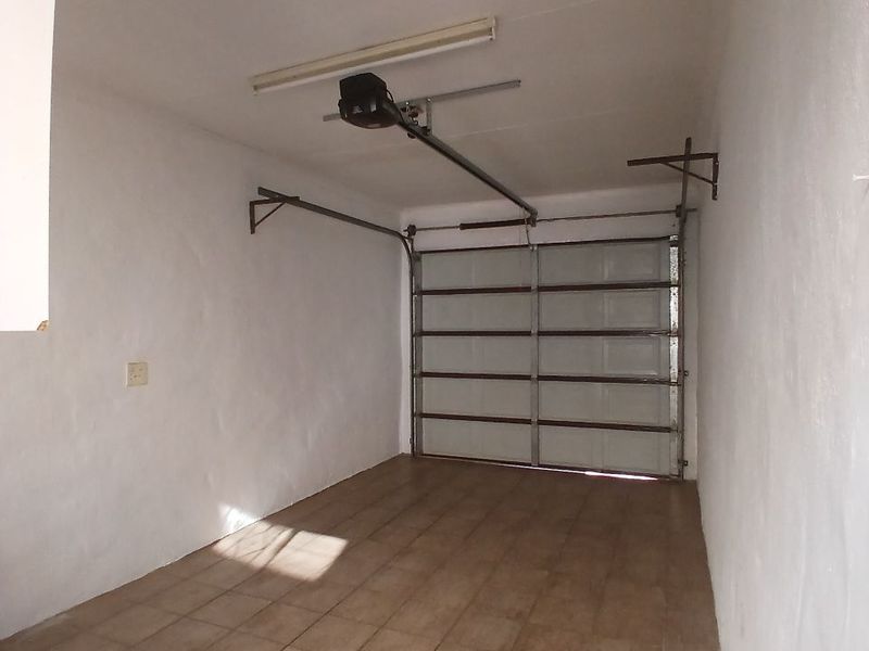 A clean, empty single-car garage featuring tiled flooring, a sectional garage door with an automated motor, and a functional overhead light fixture.