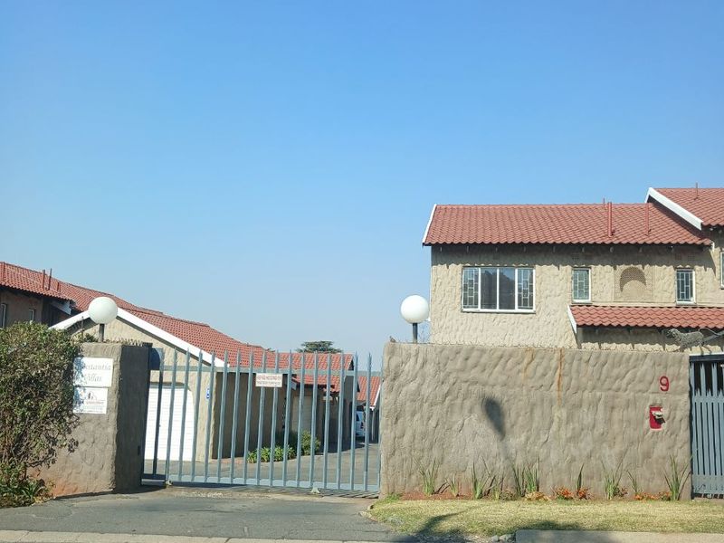 Front view of a townhouse complex entrance featuring a security gate, perimeter wall, and tiled roof architecture.