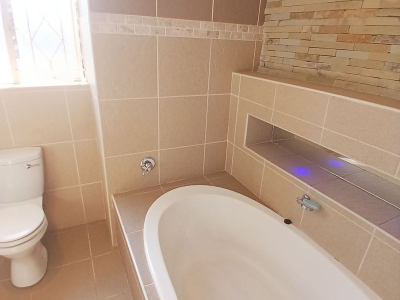 A modern bathroom featuring a built-in bathtub, a toilet, and a decorative stone feature wall with a recessed niche.