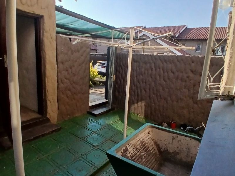 Outdoor laundry area featuring a concrete wash trough, tiled flooring, and a shade cloth awning, providing a functional utility space.