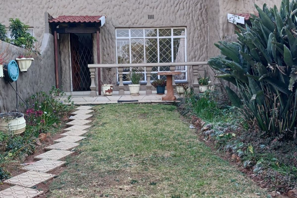 Rear view of a townhouse featuring a textured facade, a small garden with a paved walkway, and a concrete balustrade leading to the entrance.