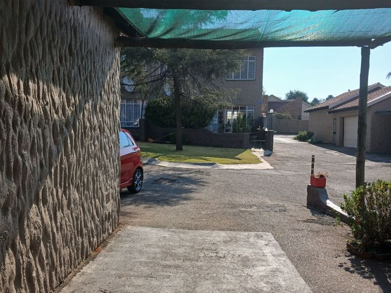 Exterior view of a townhouse driveway featuring a shaded carport structure and textured stone wall finish.