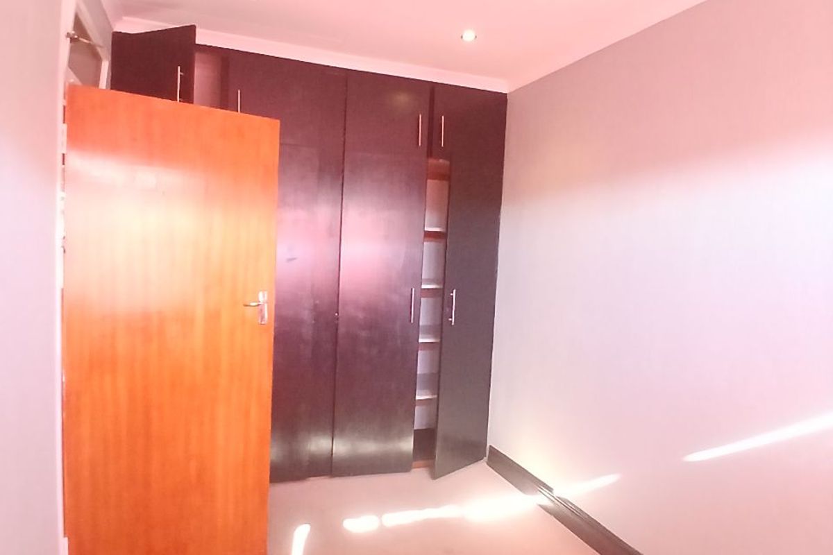 A bright, empty bedroom featuring built-in dark wood cupboards, recessed ceiling lighting, and neutral carpeting.