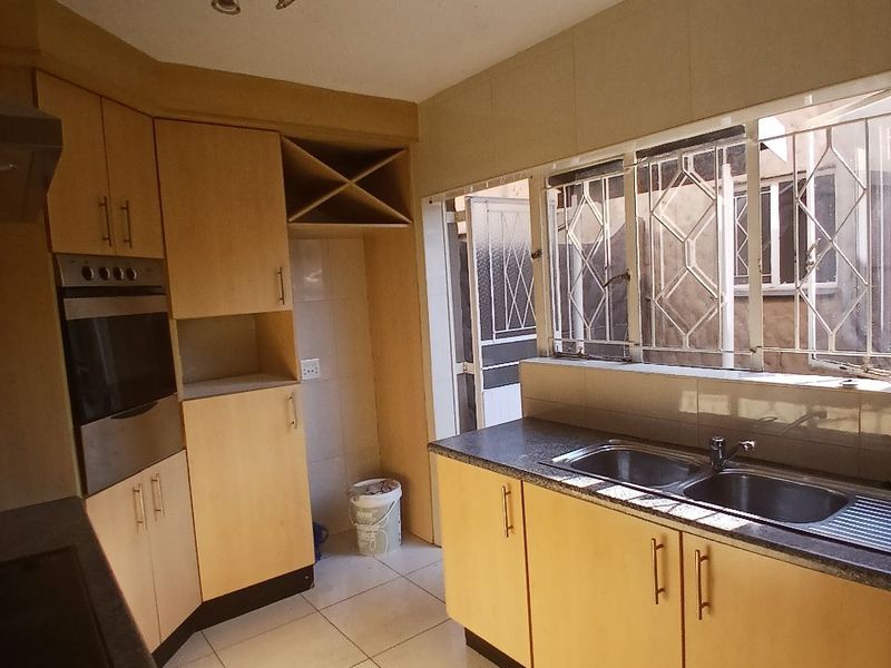 A functional kitchen featuring light wood cabinetry, built-in oven, double sink, and tiled flooring, offering a practical layout with natural light.