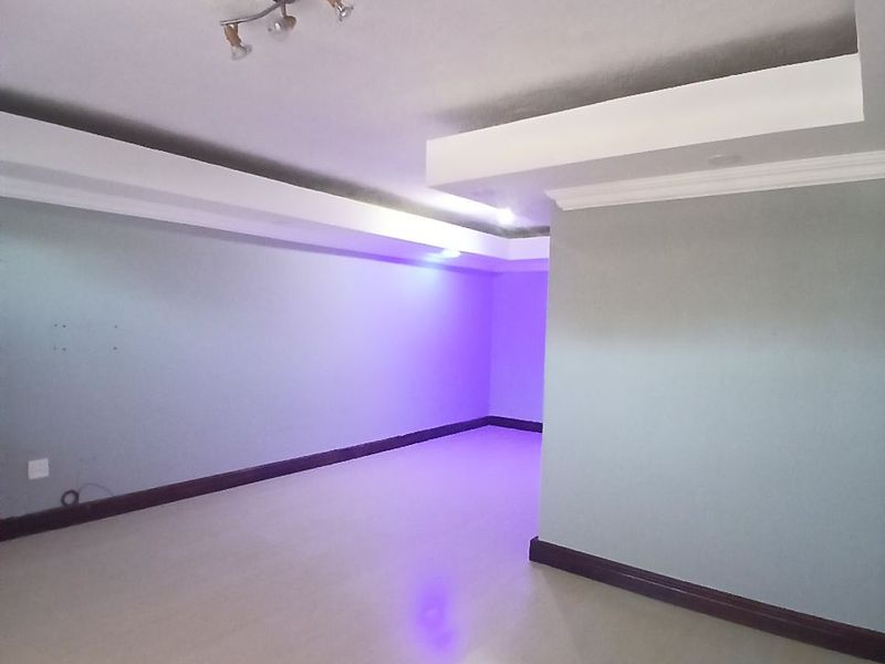 An empty living room featuring modern recessed ceiling details, cove lighting, and laminate flooring, providing a clean and versatile space.