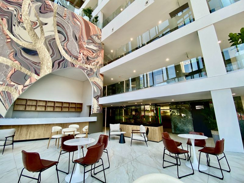 A modern, multi-level commercial atrium featuring high ceilings, glass balustrades, marble-look flooring, and a striking large-scale wall mural with integrated service counter.