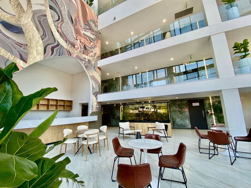 Spacious commercial atrium featuring a multi-level design, glass balustrades, marble-look flooring, and a striking feature wall mural in a modern, well-maintained lobby area.