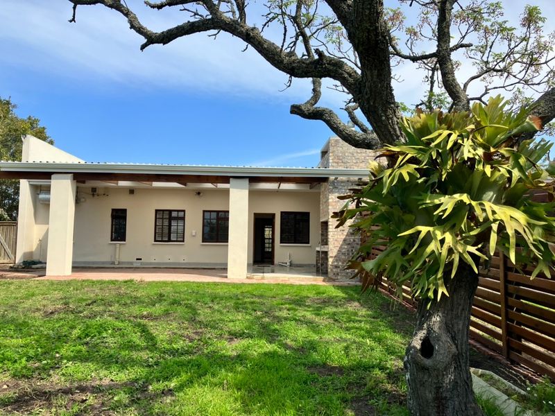 Rear view of the house featuring a covered patio with a brick fireplace, timber pergola, and access to the garden area.
