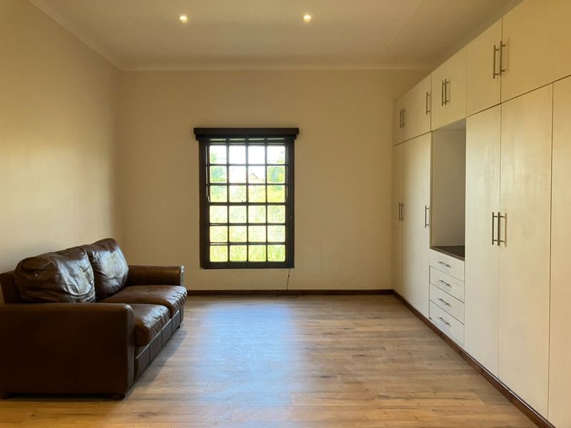 A well-maintained bedroom featuring extensive built-in cabinetry, modern laminate flooring, and recessed downlighting, offering a clean and functional living space.