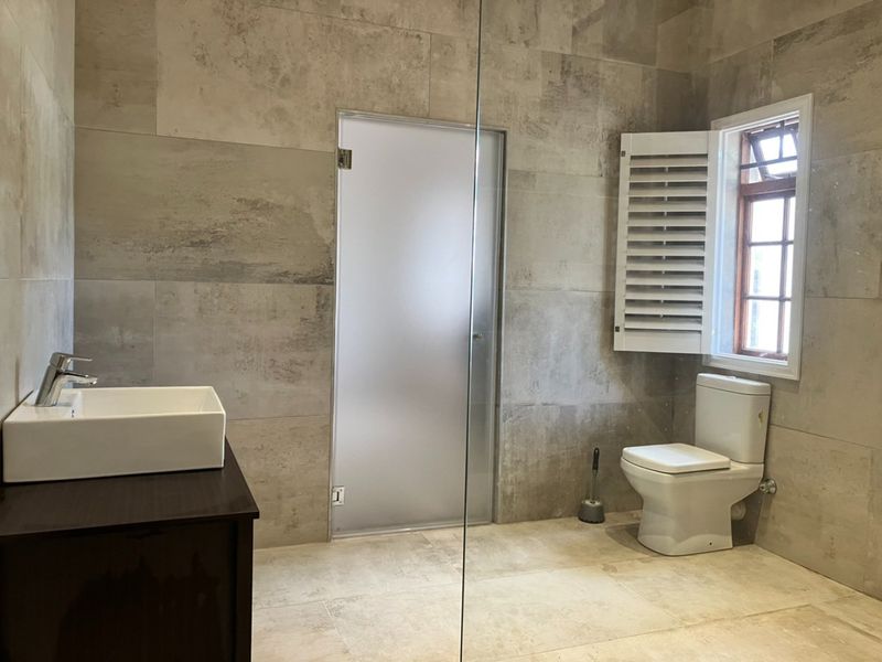 Modern bathroom featuring large format wall tiles, a vessel sink vanity, a private frosted glass door, and a toilet with plantation shutters.