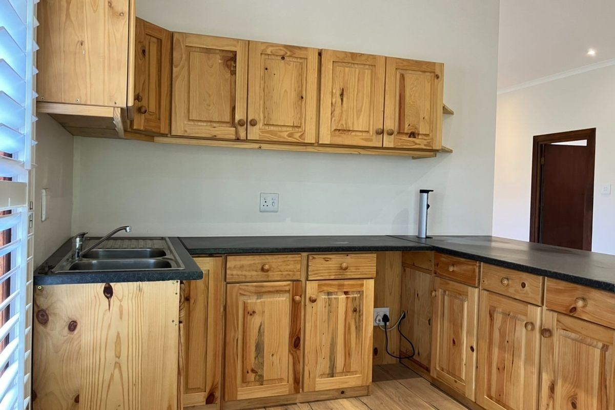 A functional kitchen featuring pine cabinetry, dark laminate countertops, and a stainless steel double sink with timber flooring.