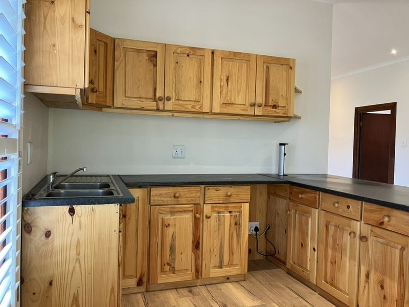 A functional kitchen featuring pine cabinetry, dark laminate countertops, and a stainless steel double sink with timber flooring.