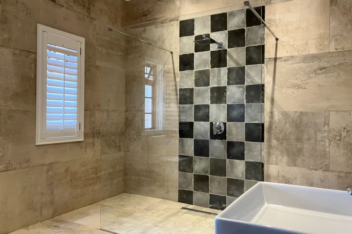 Modern bathroom featuring a spacious walk-in shower with a glass screen, rainfall shower head, and stylish checkered tile accent wall.