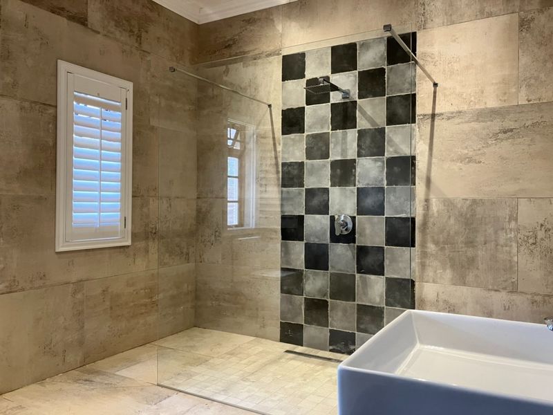 Modern bathroom featuring a spacious walk-in shower with a glass screen, rainfall shower head, and stylish checkered tile accent wall.