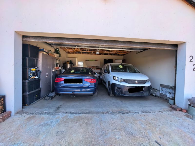 A double garage featuring exposed timber ceiling joists, concrete flooring, and built-in storage cabinetry, providing ample space for vehicle parking and utility storage.