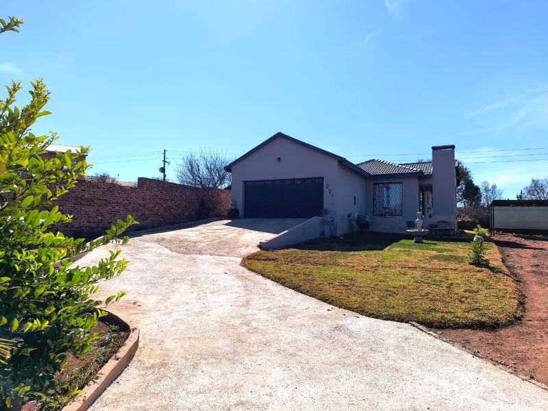 Front view of a single-story house featuring a concrete driveway, double garage, and brick boundary wall on a clear day.