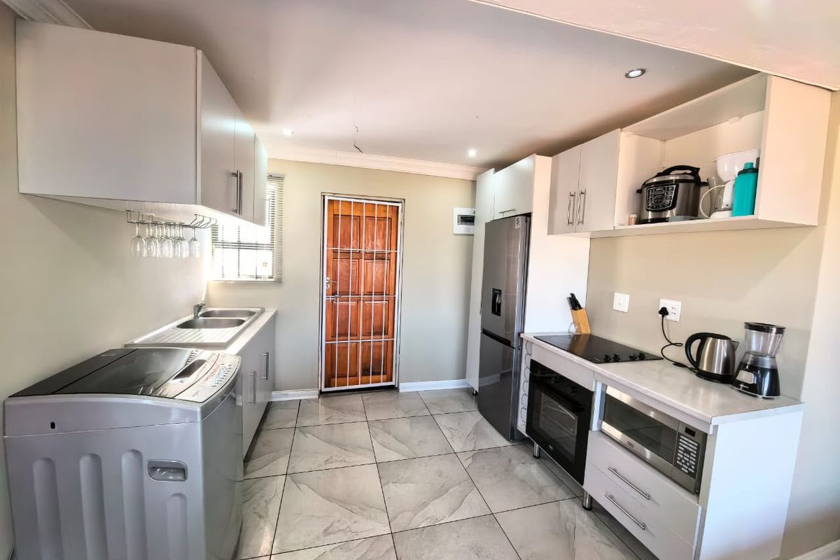 A functional kitchen featuring modern white cabinetry, tiled flooring, integrated appliances including an oven and hob, and a secure rear access door.
