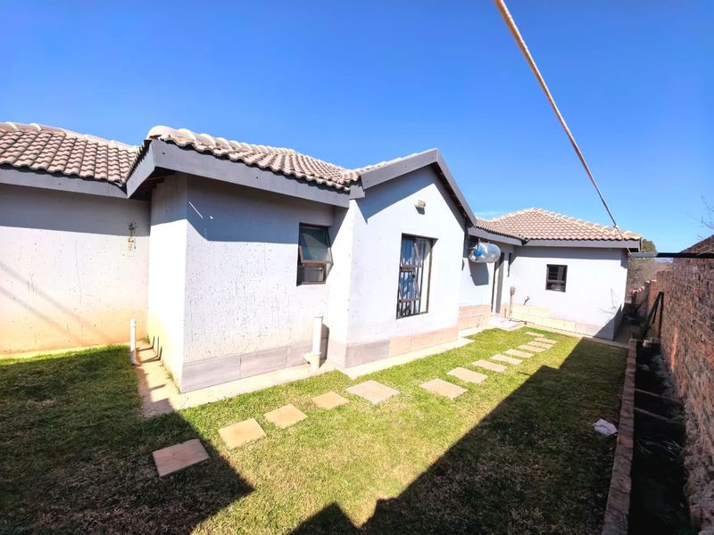 Rear view of the property featuring a small lawn, concrete stepping stones, and a brick boundary wall under a clear blue sky.