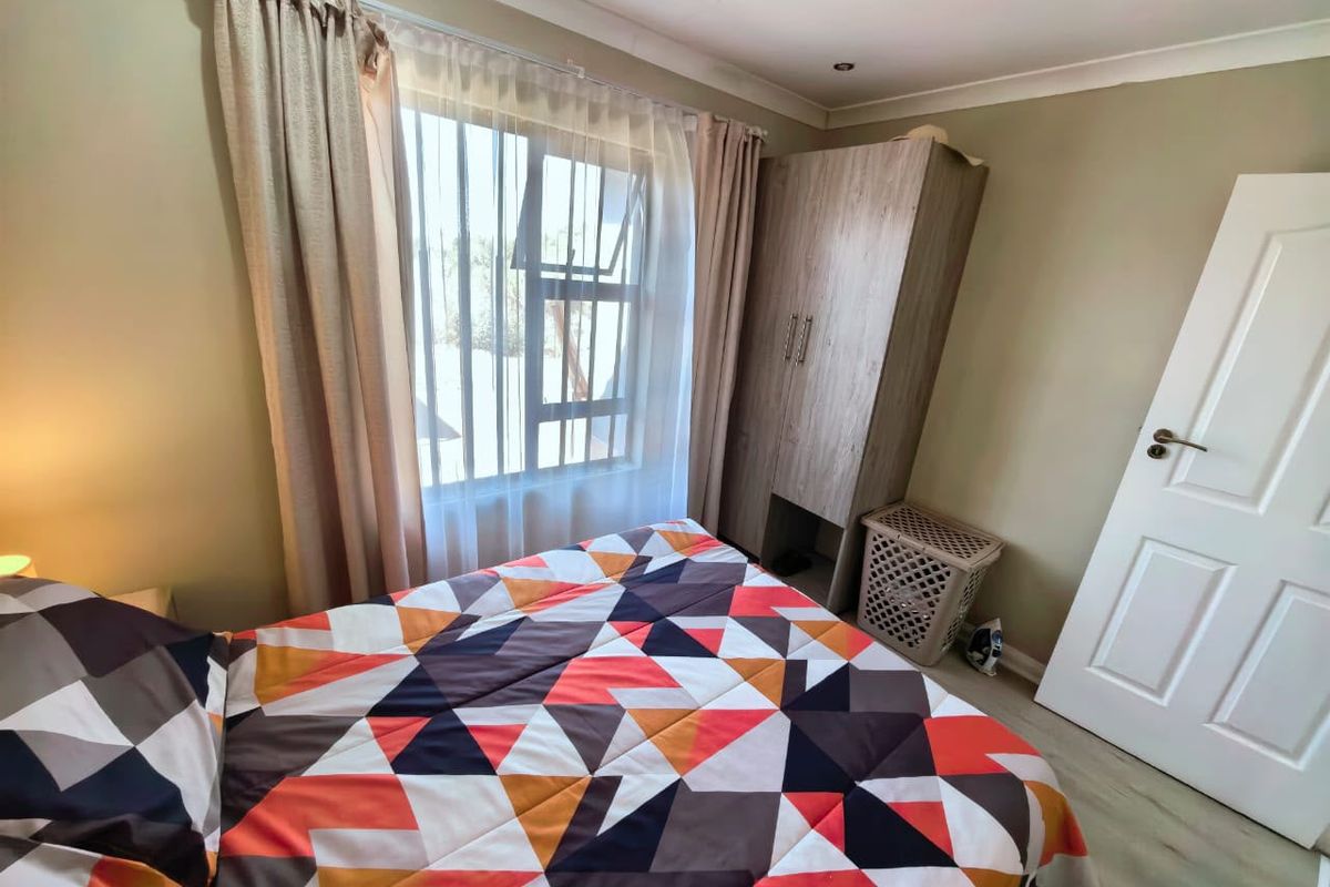 A functional bedroom featuring laminate flooring, a built-in cupboard, and an aluminium window frame, providing a comfortable and practical living space.
