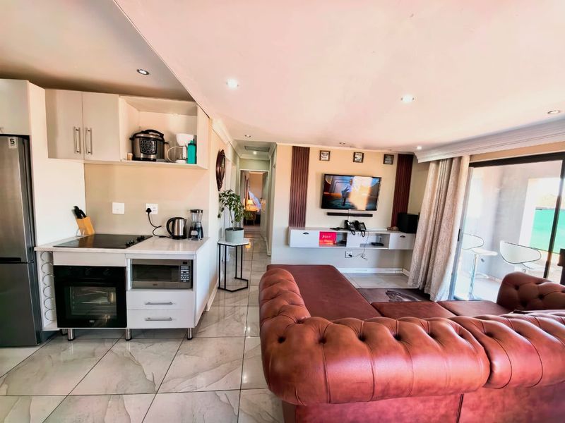 Open-plan living area featuring a modern kitchen with built-in appliances, stone countertops, tiled flooring, and direct access to an outdoor patio.
