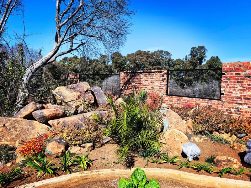 A well-maintained garden area featuring a landscaped rockery, established plantings, and a secure brick boundary wall with integrated metal fencing.