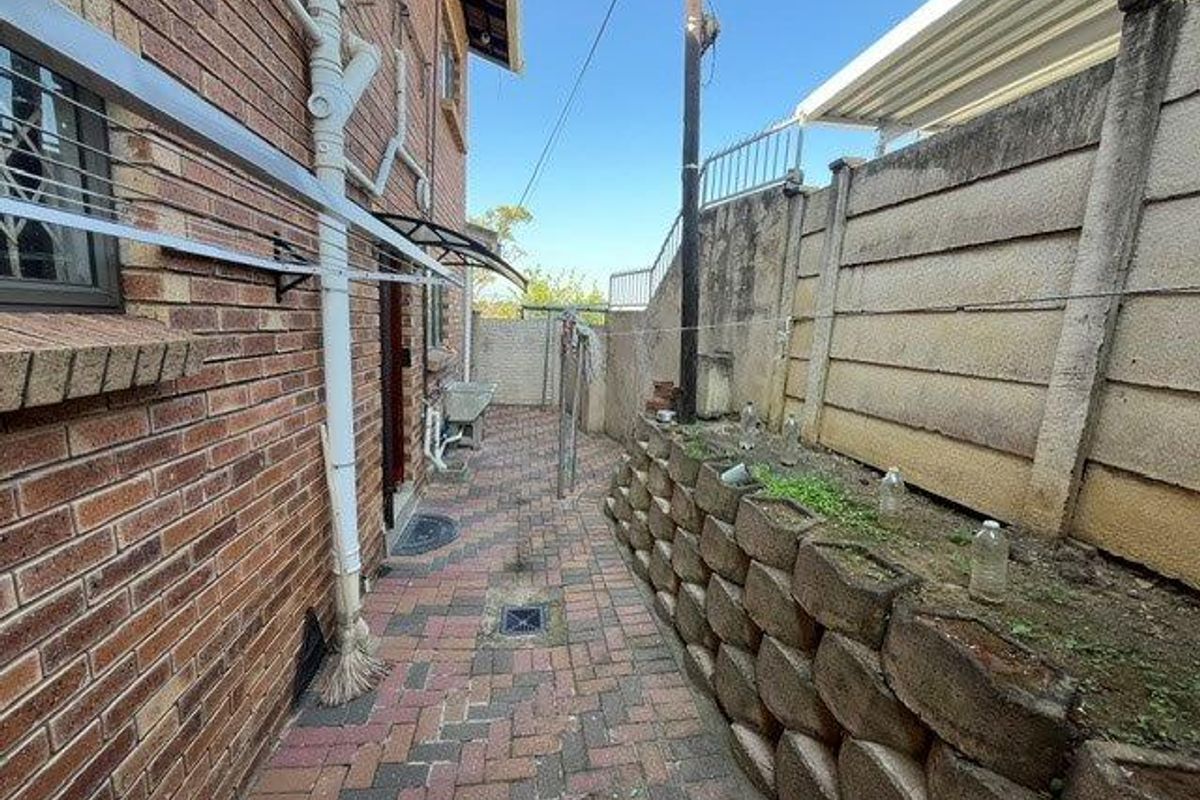 A paved side exterior area featuring a brick retaining wall, precast boundary wall, and an external utility wash basin.