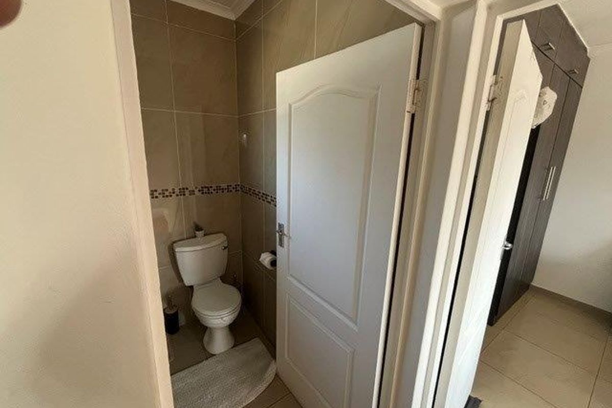 A compact bathroom featuring tiled walls and flooring, equipped with a standard toilet, adjacent to a hallway with built-in storage cupboards.