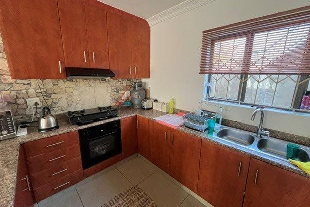 Functional kitchen featuring warm-toned cabinetry, stone-look backsplash, gas hob, built-in oven, and a double bowl sink with window views.