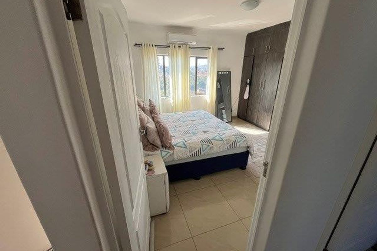A well-lit bedroom featuring tiled flooring, built-in cupboards for storage, and a wall-mounted split-system air conditioning unit.