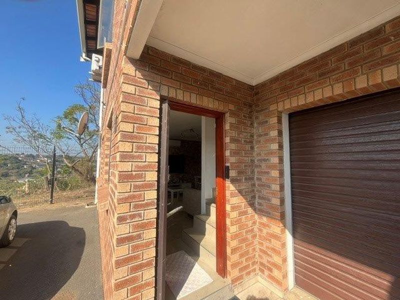 Exterior view of the property entrance featuring face brick construction, a roller garage door, and a covered entryway with concrete steps.
