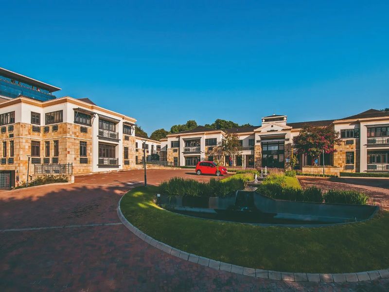 A professional exterior view of a multi-story commercial office complex featuring stone cladding, paved driveways, and a central landscaped water feature.