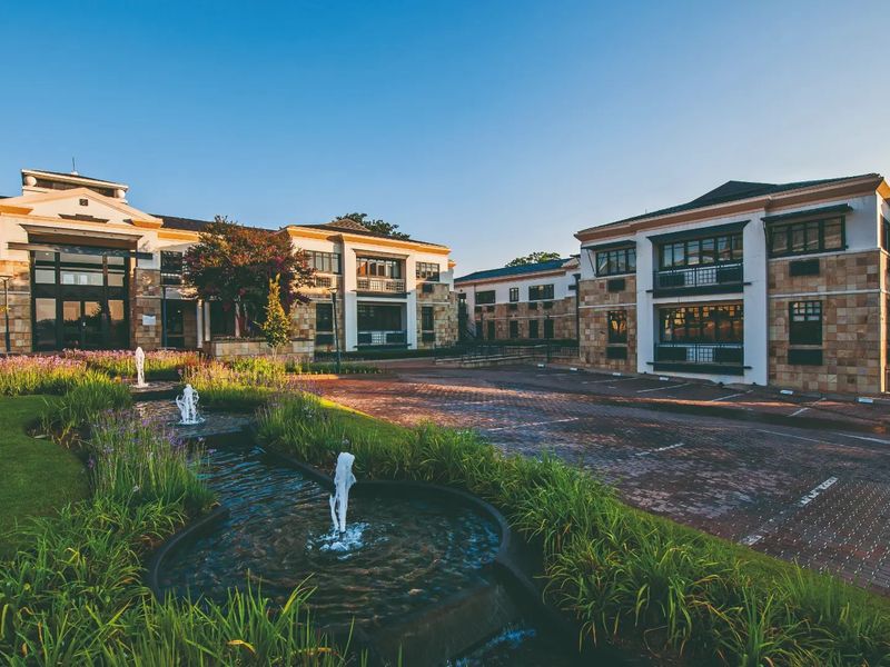 A professional exterior view of a commercial office complex featuring stone facades, paved parking areas, and a landscaped water feature in the foreground.