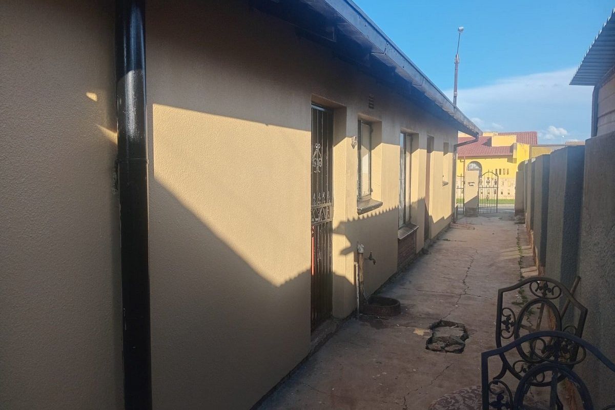 A side exterior view of the property featuring a concrete pathway, security gate, and external water tap along the boundary wall.