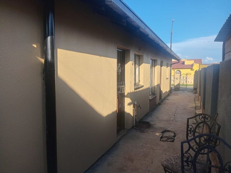 A side exterior view of the property featuring a concrete pathway, security gate, and external water tap along the boundary wall.