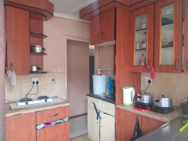 A dated kitchen featuring laminate cabinetry, tiled backsplash, and laminate countertops, requiring cosmetic updates to improve functionality and aesthetic appeal.