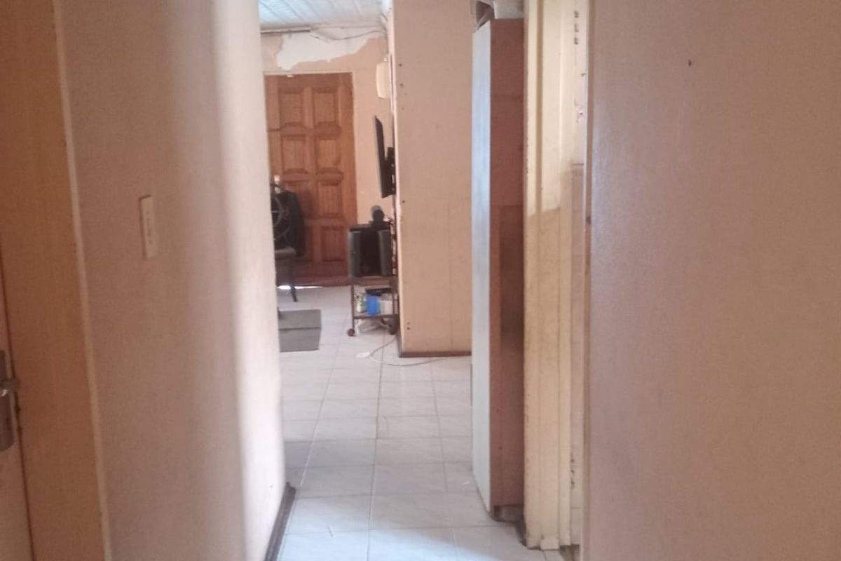 A narrow hallway featuring tiled flooring and textured ceiling tiles, showing signs of wear and requiring cosmetic updates to improve the overall condition.