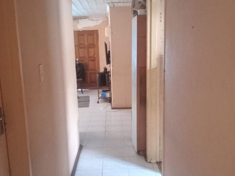 A narrow hallway featuring tiled flooring and textured ceiling tiles, showing signs of wear and requiring cosmetic updates to improve the overall condition.