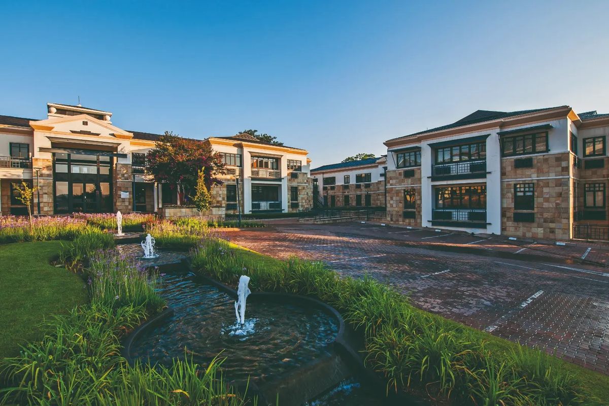 A professional exterior view of a commercial office complex featuring stone facades, paved parking areas, and a landscaped water feature in the foreground.
