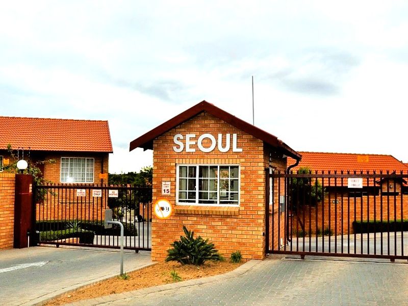 The entrance to the Seoul townhouse complex featuring a brick security gatehouse, metal access gates, and paved driveway.