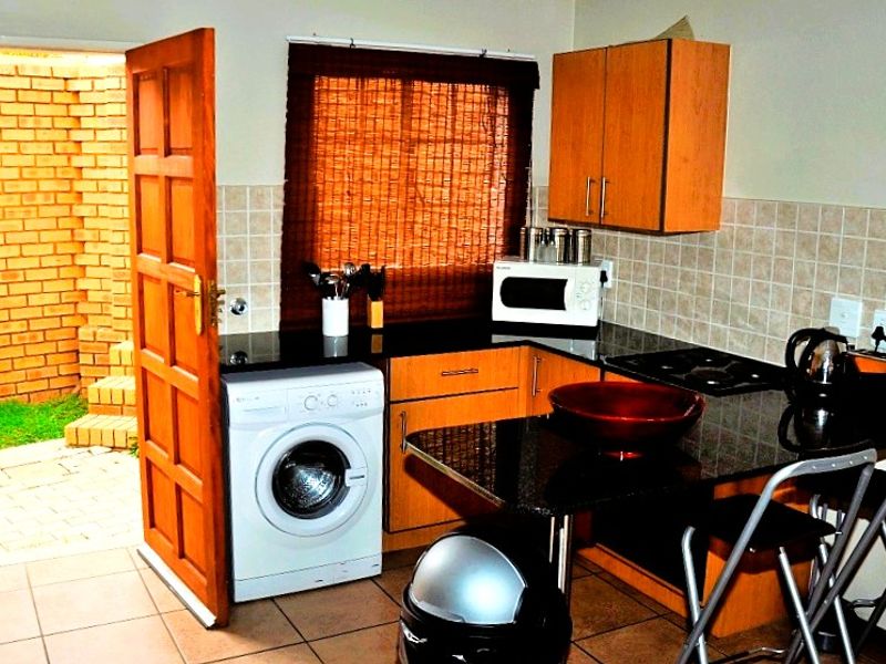 Compact kitchen featuring wooden cabinetry, granite countertops, tiled backsplash, and a built-in washing machine, with direct access to an outdoor courtyard area.
