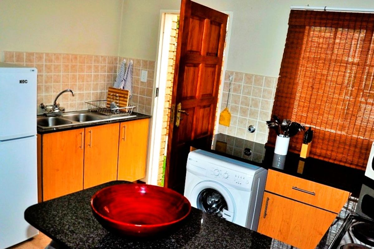 Functional kitchen featuring granite countertops, tiled backsplash, double sink, and dedicated space for laundry appliances with direct access to the exterior.