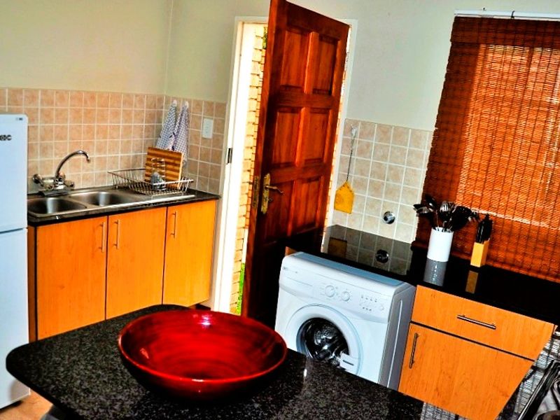 Functional kitchen featuring granite countertops, tiled backsplash, double sink, and dedicated space for laundry appliances with direct access to the exterior.