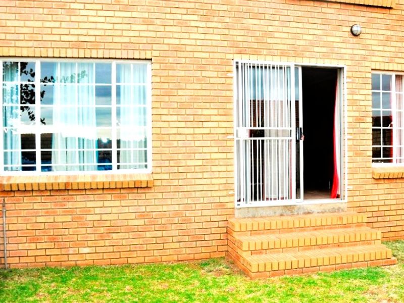 Rear exterior view of the townhouse featuring a face brick facade, sliding glass door with security gate, and brick steps leading to the garden.