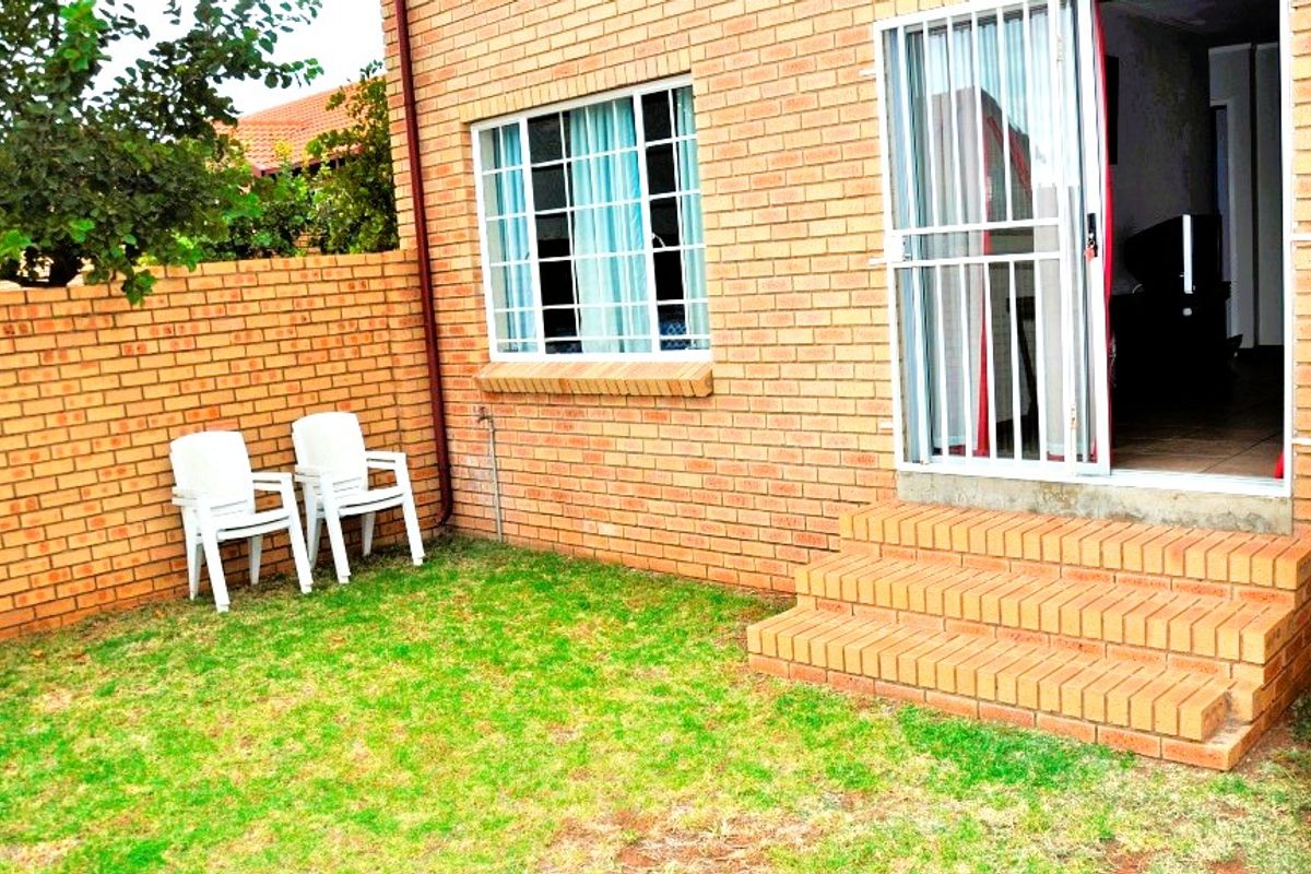 Rear exterior view of the townhouse featuring face brick walls, a security gate entrance, and brick steps leading into the home.